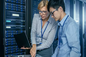 Female professor with laptop assisting male student with computer hardware 