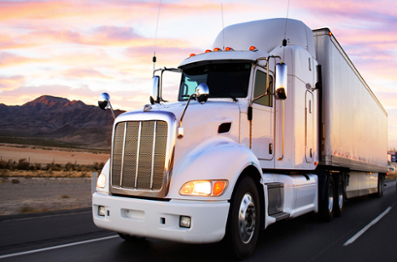 Image of a white truck on the road with a pink and purple sky, and mountains in the background 